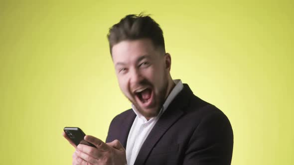 Overjoyed Young Man in Office Suit Looking on Smartphone Doing Winner Gesture