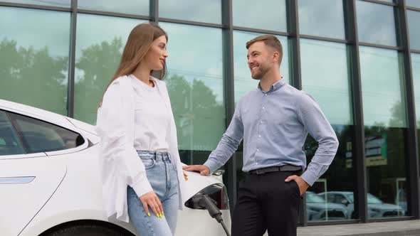 Young Couple Man and Woman Traveling Together By New Car Having Stop at Charging Station alt