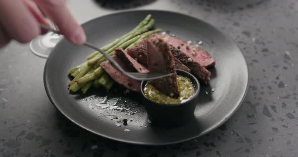Slow Motion Man Eat Sliced New York Steak with Roasted Asparagus on Black Plate alt
