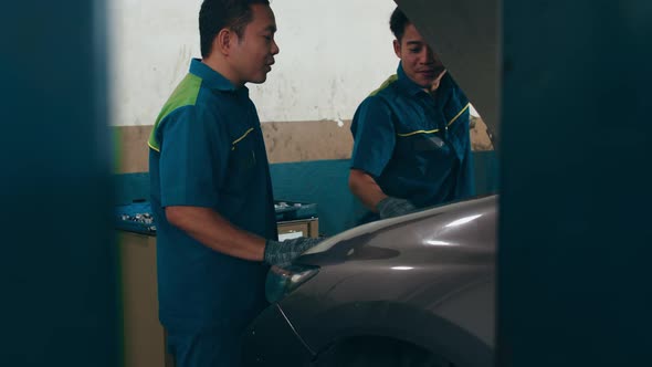 Skillful Asian guy in uniform fixing car at mechanics garage at night.