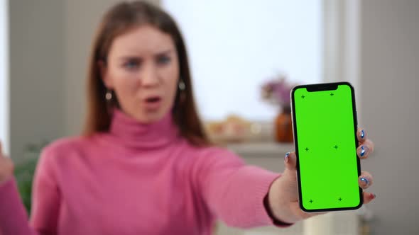 Smartphone with Green Screen and Blurred Surprised Caucasian Woman Gesturing Saying Wow at alt
