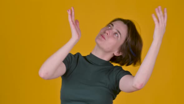 Young cheerful girl in t-shirt smiling dancing and looking at the camera on yellow studio background