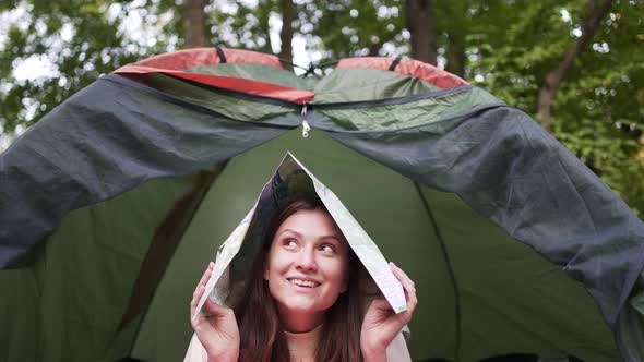 A Female Tourist Fools Around with a Map in a Tent in the Woods
