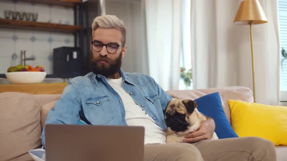 Man Freelancer Working at Home Office with Laptop and Pug Dog on Arms alt