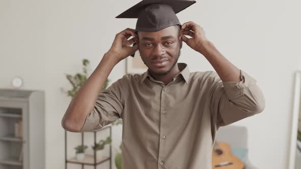 Portrait of Young African-American Man Putting on Graduation Cap alt