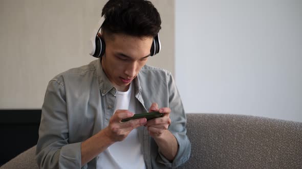 Focused Asian Man Enjoys Playing Racing Game on Smartphone alt