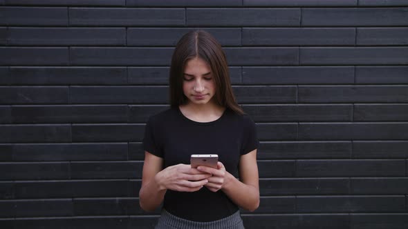 An Attractive Young Lady Wearing Glasses Using a Phone Against a Brick Wall Background. Close-up alt