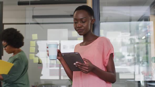 African american businesswoman drinking takeaway coffee using tablet and smiling to camera in office alt