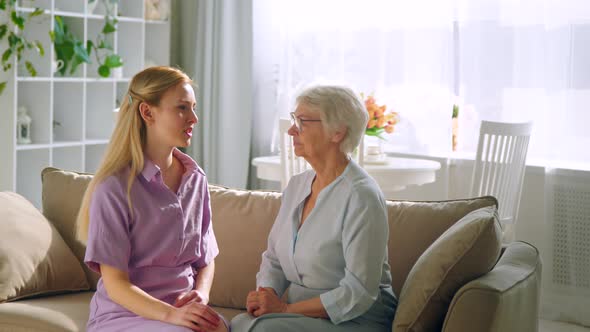 A young girl and an elderly woman are talking on the couch in a bright room alt