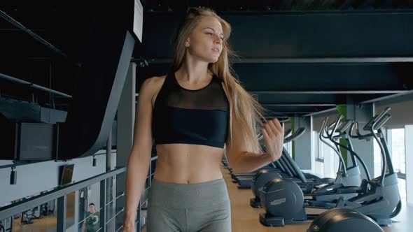 Confident Slim Young Ahlete Woman Walking By Trainer Equipment in Gym.