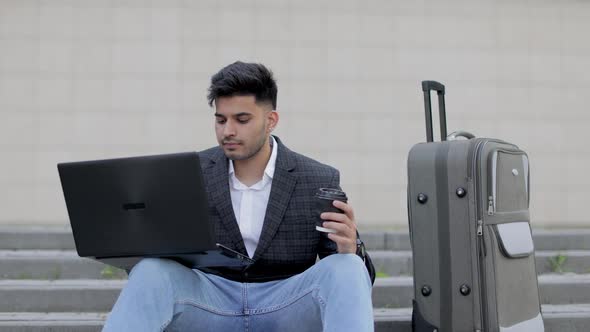 Young Handsome Bearded Asian Indian Man in Smart Casual Clothes with Wireless Laptop Sitting on alt