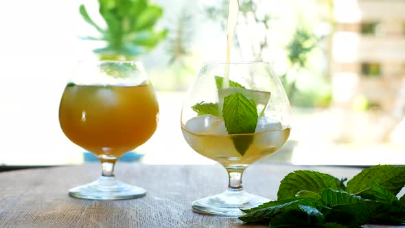 Pouring kombucha into a glass with ice and mint leaves; bright backlit alt