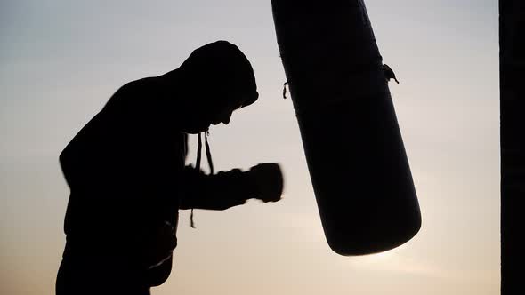 Boxer beats punching bag on sunset background. Silhouette motivation sport boxing. Epic video. alt