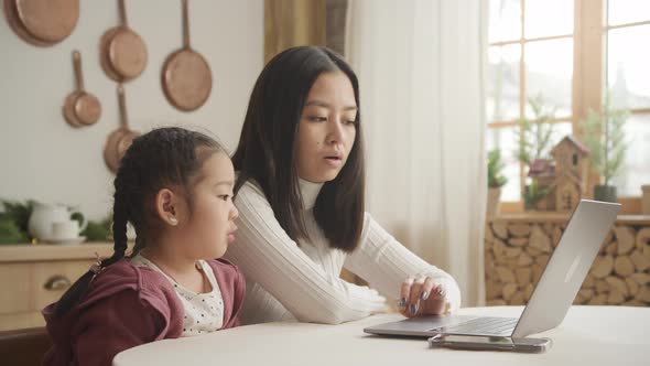 Mother Teaching Her Daughter a Lesson on a Laptop Indoors alt