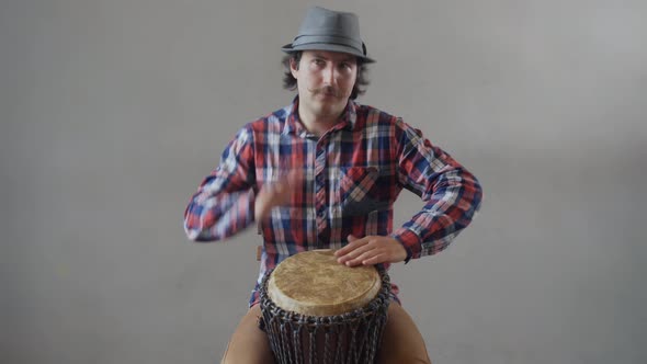Funny Man with a Mustache and a Hat Playing the Ethnic Drum