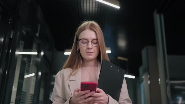 Portrait of a Business Woman with Glasses Walking in the Office Corridor and Answering in a Mobile alt