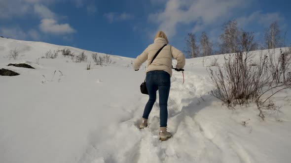 A Tourist Girl in a Beige Jacket and Trekking Boots Climbs a Snowy Mountain