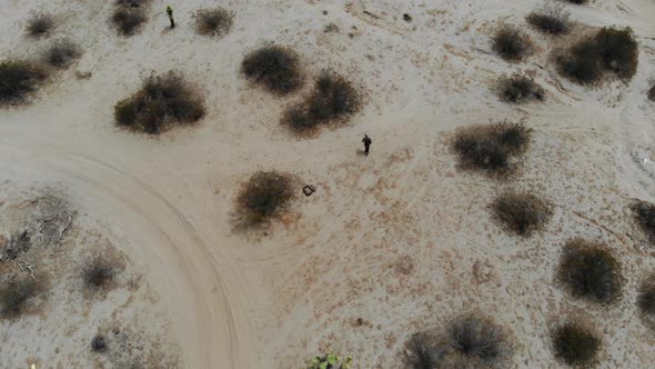 A Man walks slowly on his own through the barren lonley desert in Joshua Tree birdseye Drone Aerial, alt