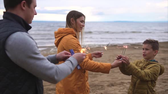Young Family with the Son Burn the Bengal Lights Near the Sea in the Open Air alt
