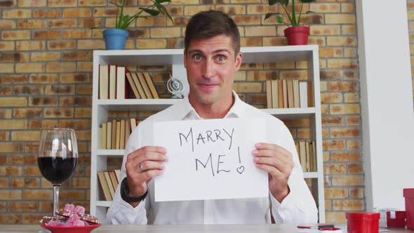 Caucasian man making video call holding handwritten sign making marriage proposal and celebrating ac alt