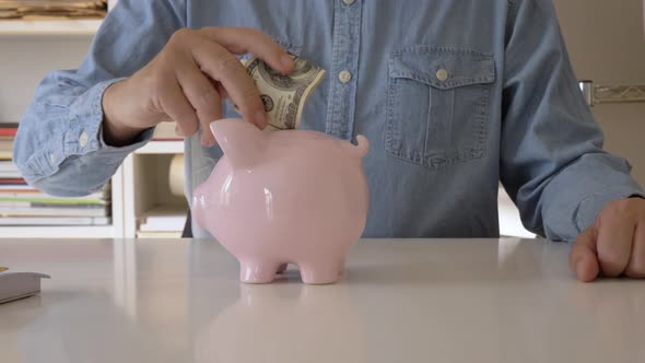 Man Introducing One Hundred Dollars in Piggy Bank