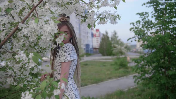 A Cute Girl with Dreadlocks Poses By a Tree with Leaves