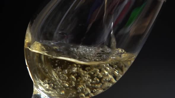 Wine is poured into a glass on a black background. Slow motion. alt