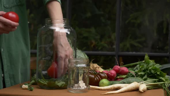woman prepares tomatoes for canning in jar next to a window on background