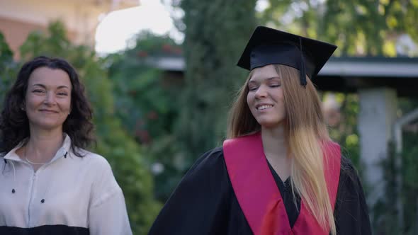 Confident Mature Mother and Grad Daughter Walking in Slow Motion on Front Yard on Graduation Day alt