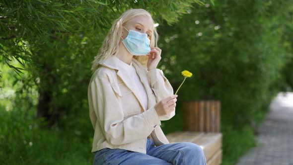 The Woman Takes Off Her Medical Mask and Sniffs the Yellow Dandelion alt