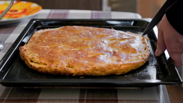 Caucasuan Hands Slicing Freshly Baked Domestic Ossetian Pie on a Baking Sheet with Kitchen Knife alt
