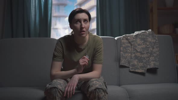 Young Military Woman Sits on the Sofa and Covers Her Face with Her Hands alt