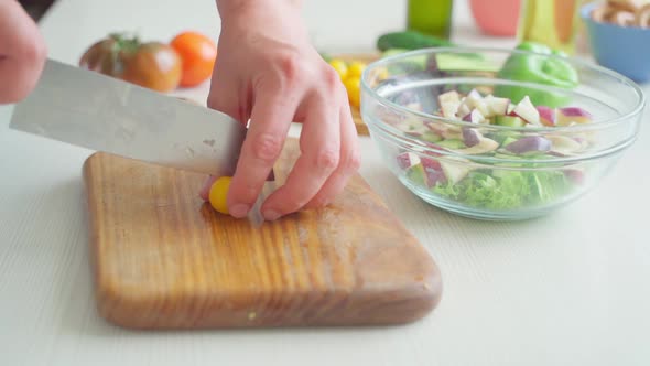 Male Hands are Cutting Small Yellow Cherry Tomatoes on a Cutting Board alt