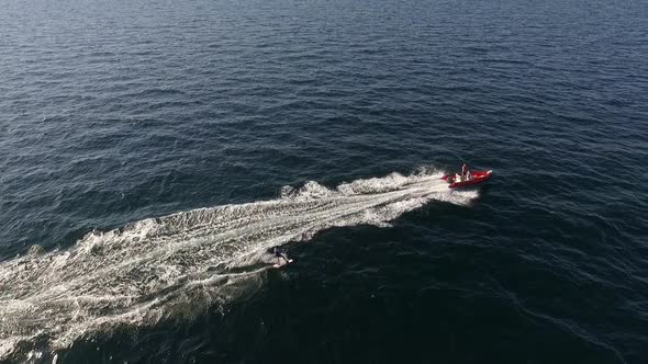 Flyover Drone Footage of Red Inflatable Boat Pulling Male on Board in Sea in Slowmotion alt