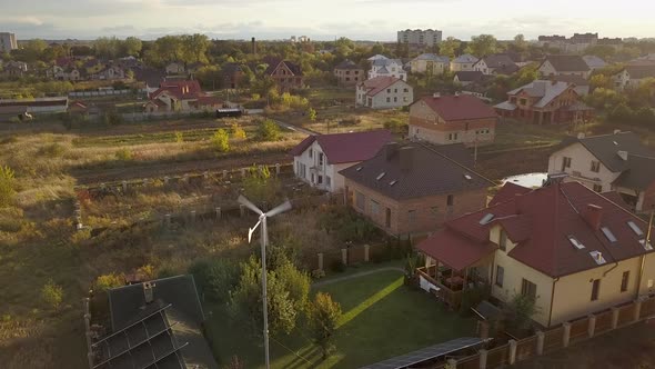 Aerial view of a residential private house with solar panels on roof and wind generator turbine. alt