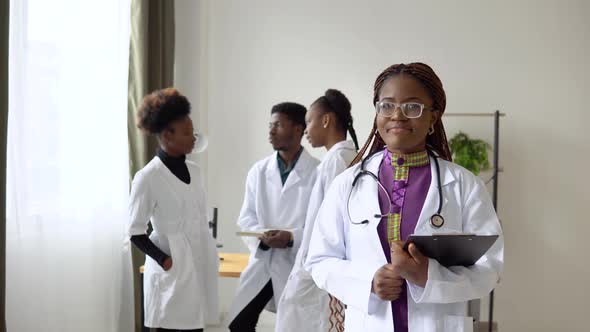 A Young African American Female Doctor Stands in Front and Looks at the Camera Against  alt
