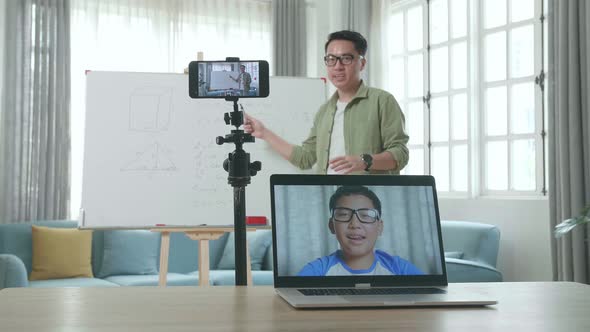 Male Teacher Shoots Video By Smartphone While Having Video Call On Laptop And Teaching Math At Home alt