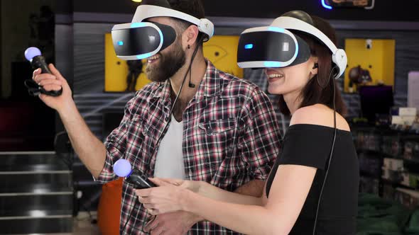 Man and Woman Use a Virtual Reality Headset with Glasses and Hand Motion Controllers and Weapons