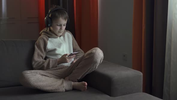 The Guy in the Headphones and with the Smartphone in His Hands Sits on the Couch Listening To Music
