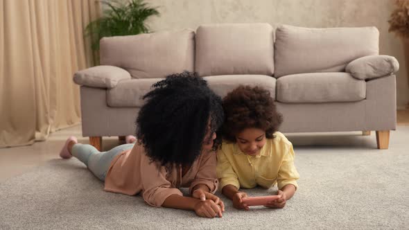 Little African American Girl Plays Game on Smartphone and Rejoices Victory alt
