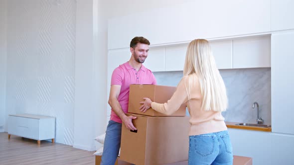 Young woman blonde with long loose hair helps bearded man carry large brown boxes alt