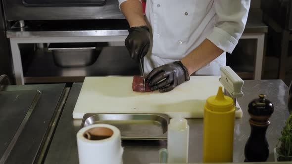 Male Chef Cutting Piece of Beef on Wooden Board in Restaurant Kitchen alt