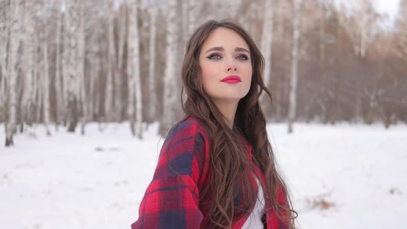 Young Woman with Wavy Hair Standing and Touching Face in Winter Forest