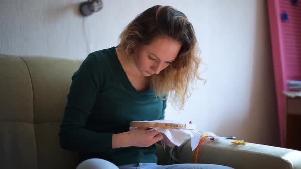 the camera moves next to a girl embroidering a picture on the canvas alt