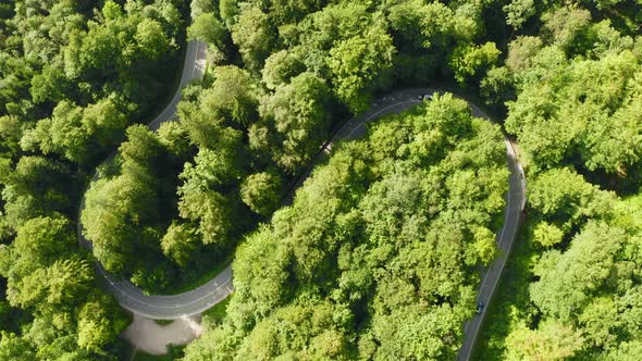 Timelapse from above: Cars a driving through a double curve in a summertime forest, fast dynamic vid alt