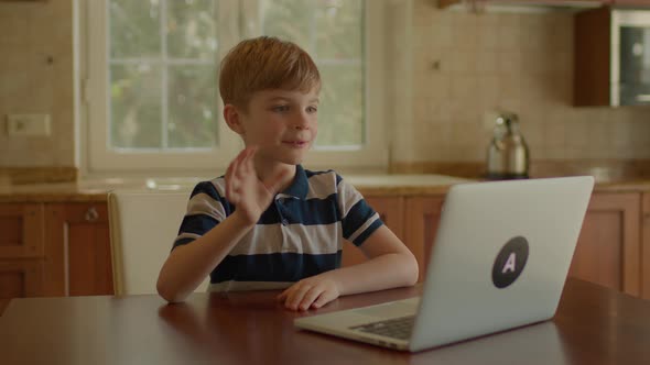 School Boy Learning Online Using Laptop Sitting in the Kitchen at Home alt