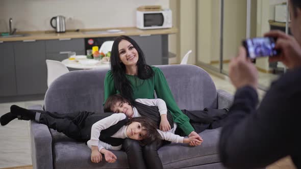 Wide Shot of Happy Smiling Caucasian Mother Posing with Middle Eastern Twin Sons Sitting on Couch As alt