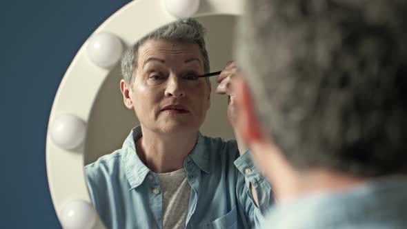 An Elderly Woman Caring for Her Appearance Tints Her Eyelashes While Sitting in Front of a Mirror at