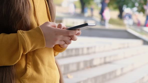 A Teenage Girl Uses a Smartphone Types Text on Her Phone and Drives Her Fingers Across the Screen alt