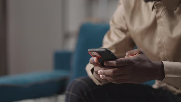 Young Black Man is Using Smartphone at Home Browsing Internet Sites Viewing Social Netscloseup View alt